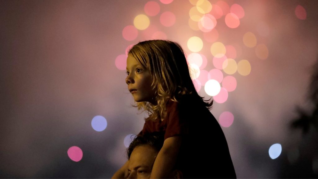 Young child sitting on adult's shoulders watching fireworks (© Julio Cortez/AP Images)